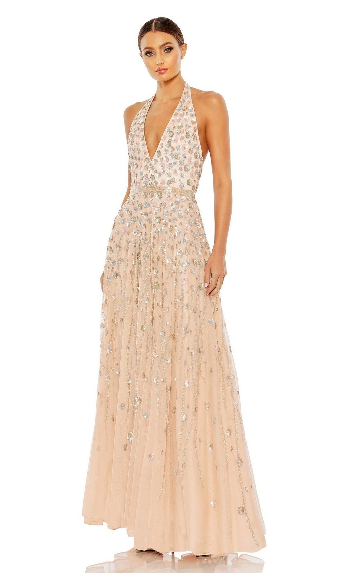 A woman wears the Long Formal Dress 5654 by Mac Duggal, a floor-length blush halter dress with a deep V-neck, sparkling sequins, and delicate floral beading for an elegant look.